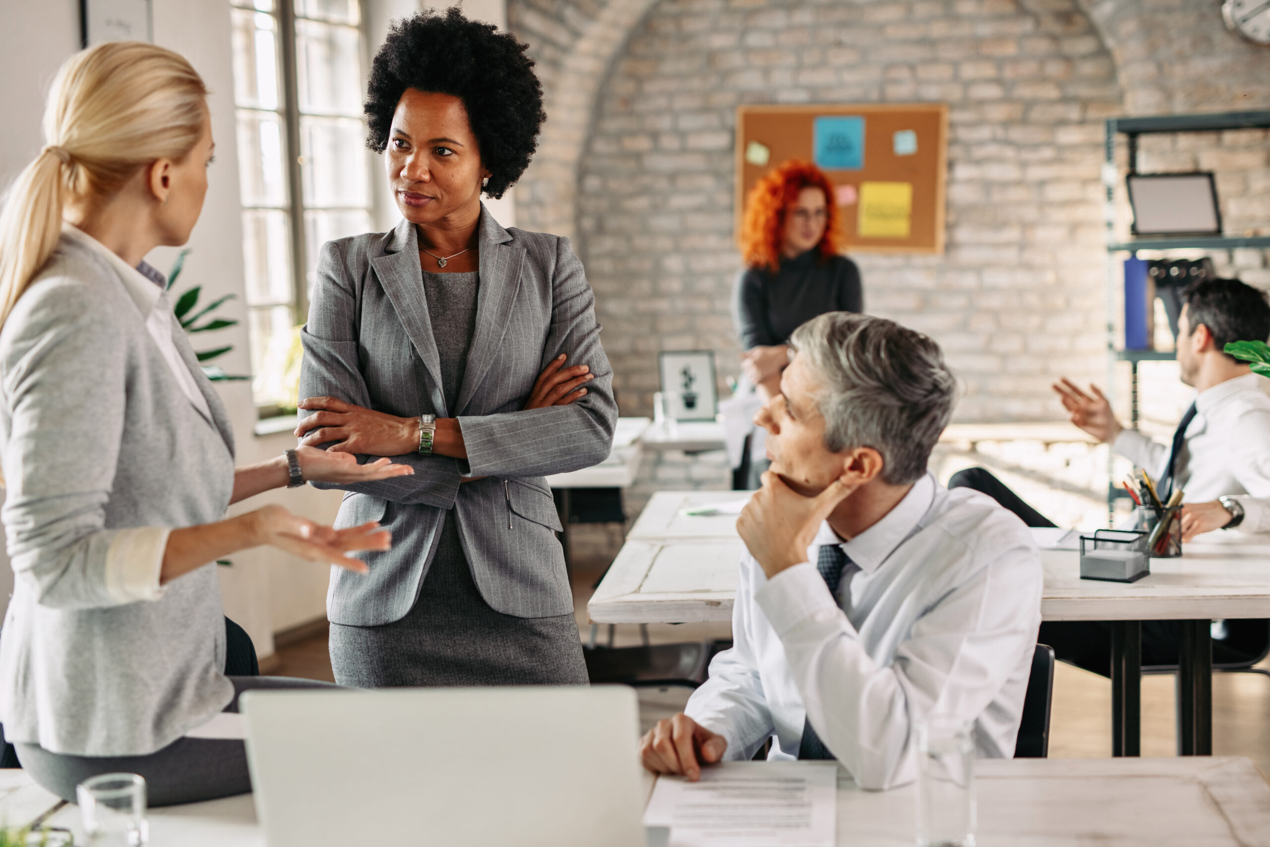 Female African American entrepreneur and her colleagues communicating on a business meeting in modern office. There are people in the background.